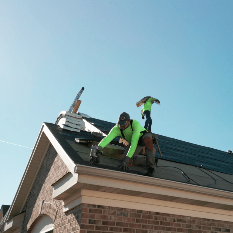 Three construction workers on a pitched roof in neon-green shirts, with a ladder and tools, under a clear blue sky.